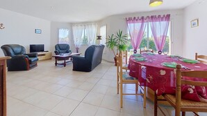 Un vaste espace de vie comprenant une table à manger pour quatre personnes, un téléviseur et des sièges confortables.