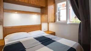 Une chambre à coucher avec une tête de lit en bois, un lit recouvert d’une couverture à carreaux, une table de chevet, une commode et une fenêtre avec des rideaux.