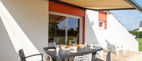 An outdoor patio with a table set for dining, surrounded by chairs, under a striped awning.