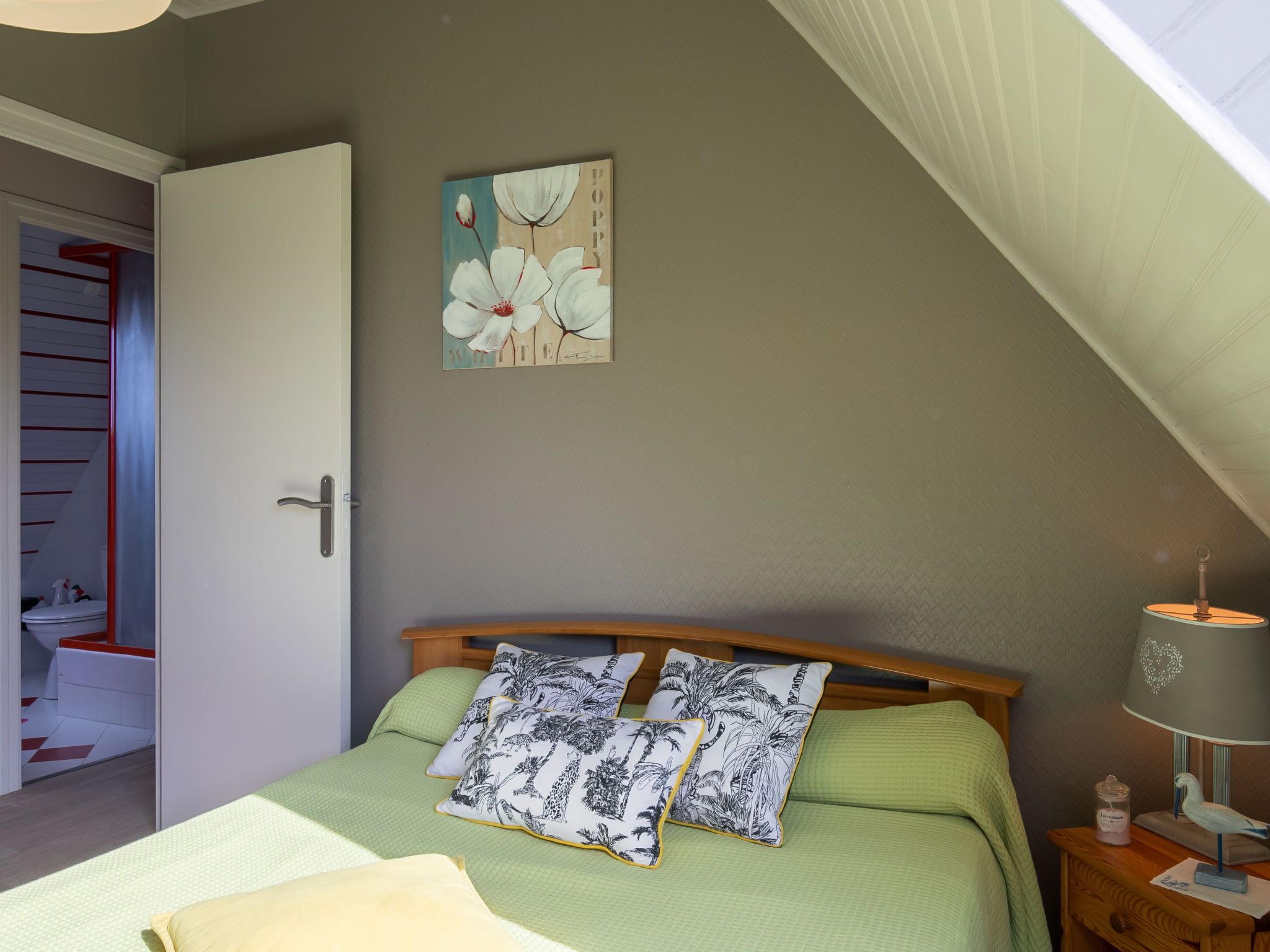 A bedroom with a bed, pillows, a nightstand, a lamp, a painting, and a closet.
