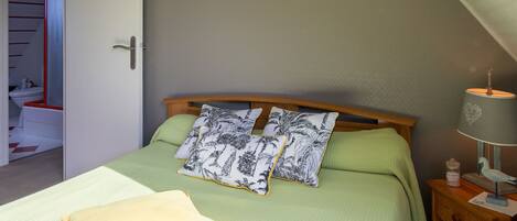 Un dormitorio con cama, almohadas, una mesita de noche, lámpara, un cuadro y un armario.