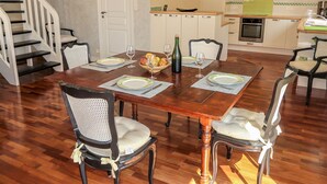 A dining area with a wooden table set for four, surrounded by upholstered chairs with white cushions. A kitchen is visible in the background with a stove, oven, and a coffee maker on the counter. - Ty Coat Pin by Interhome (Tregunc)