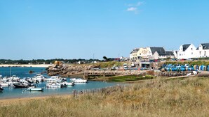 A coastal town with a marina filled with boats, a sandy beach, and several buildings including a prominent white structure with a sign. - Ty Coat Pin by Interhome (Tregunc)