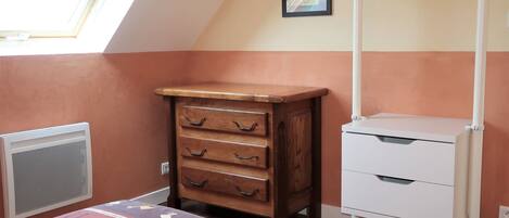Une pièce avec un plafond en pente, une commode en bois avec des tiroirs, une armoire blanche, un radiateur et un tapis à motifs.