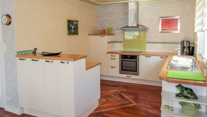 A modern kitchen with white cabinets, a wooden countertop, a built-in oven, and a green backsplash. - Ty Coat Pin by Interhome (Tregunc)