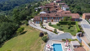 Oversigtsbillede af en villa med swimmingpool, omgivet af frodig vegetation og etageejendomme.