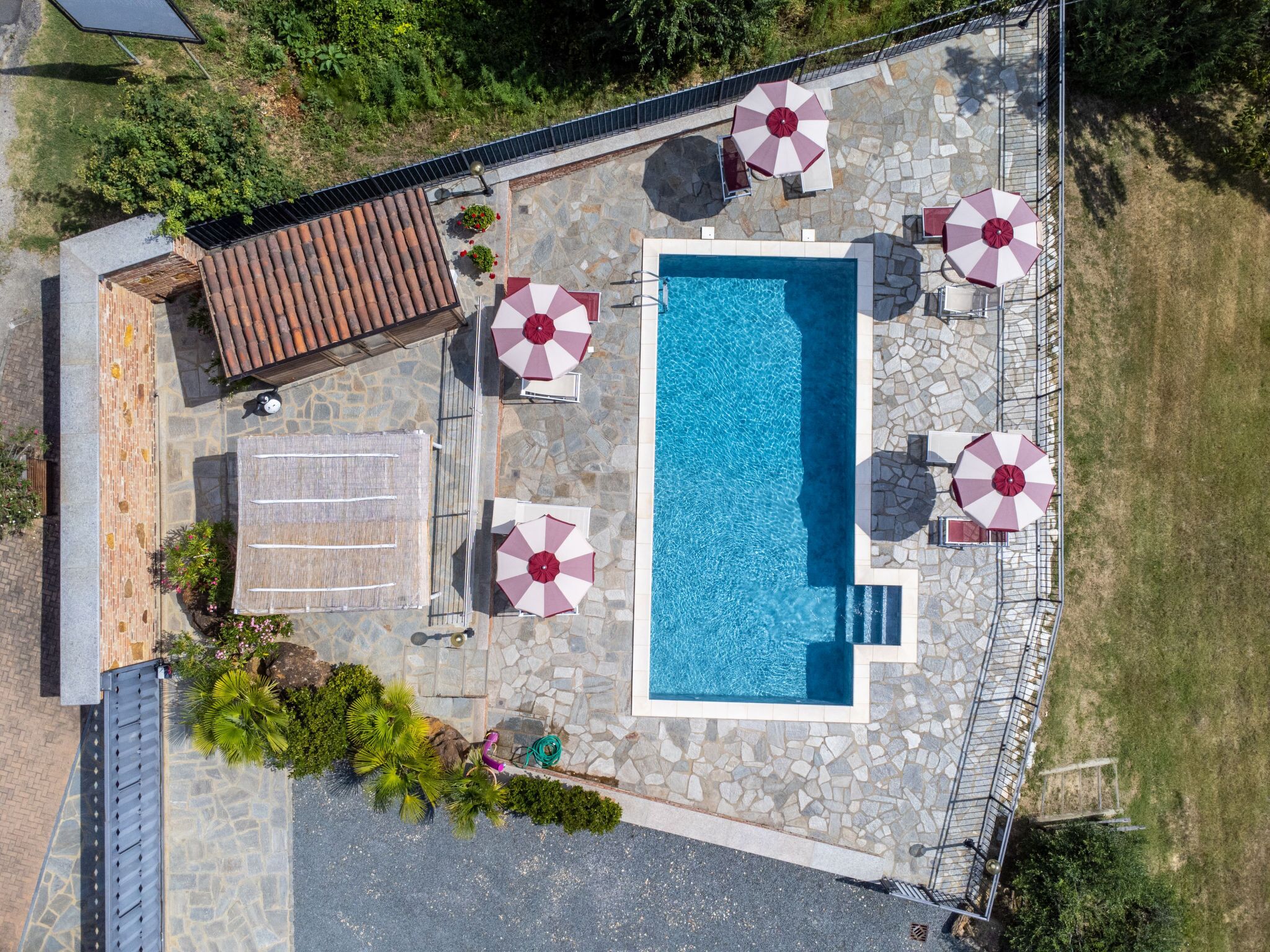 Vista aérea de una zona de piscina con suelo de piedra, rodeada de sombrillas y contigua a un edificio de ladrillo.
