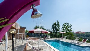 En swimmingpool med stendæk, liggestole og parasoller.