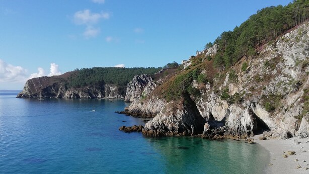 Paisagem costeira com águas azuis cristalinas, falésias rochosas e uma praia arenosa.