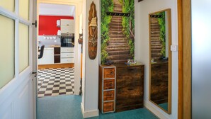 A hallway with a checkered floor, a kitchen with white cabinets, and a staircase with a green wall mural. - l'Atlantique by Interhome (Crozon-Morgat)