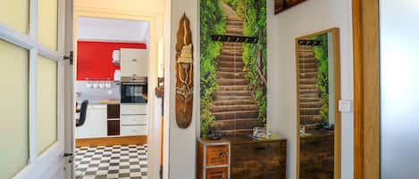 A hallway with a checkered floor, a kitchen with white cabinets, and a staircase with a green wall mural.