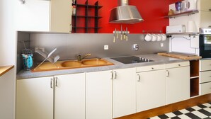 A kitchen with white cabinets, a red accent wall, stainless steel appliances, and a black and white checkered floor. - l'Atlantique by Interhome (Crozon-Morgat)