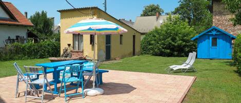 A patio area with a table and chairs, a small shed, and a house with a yellow exterior.