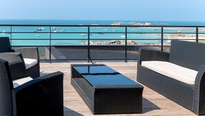 A balcony with wicker furniture overlooking a coastal area with boats and rocky formations. - De la Digue by Interhome (Plouescat)
