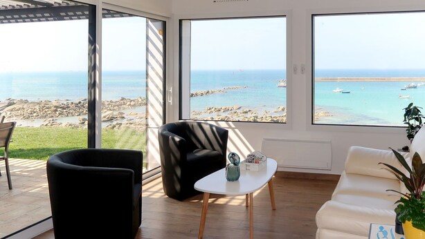A modern living room with a view of the sea, featuring a black armchair, a white sofa, and a small table with a decorative item. - De la Digue by Interhome (Plouescat)