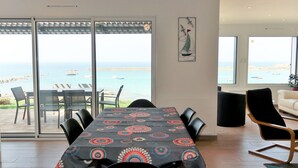 A dining area with a table covered in a patterned tablecloth, black chairs, and a view of the sea through large glass doors. - De la Digue by Interhome (Plouescat)