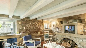 A stone-walled living room with a fireplace, a dining area, and a view of the outdoors. - Kermalo by Interhome (Plouescat)