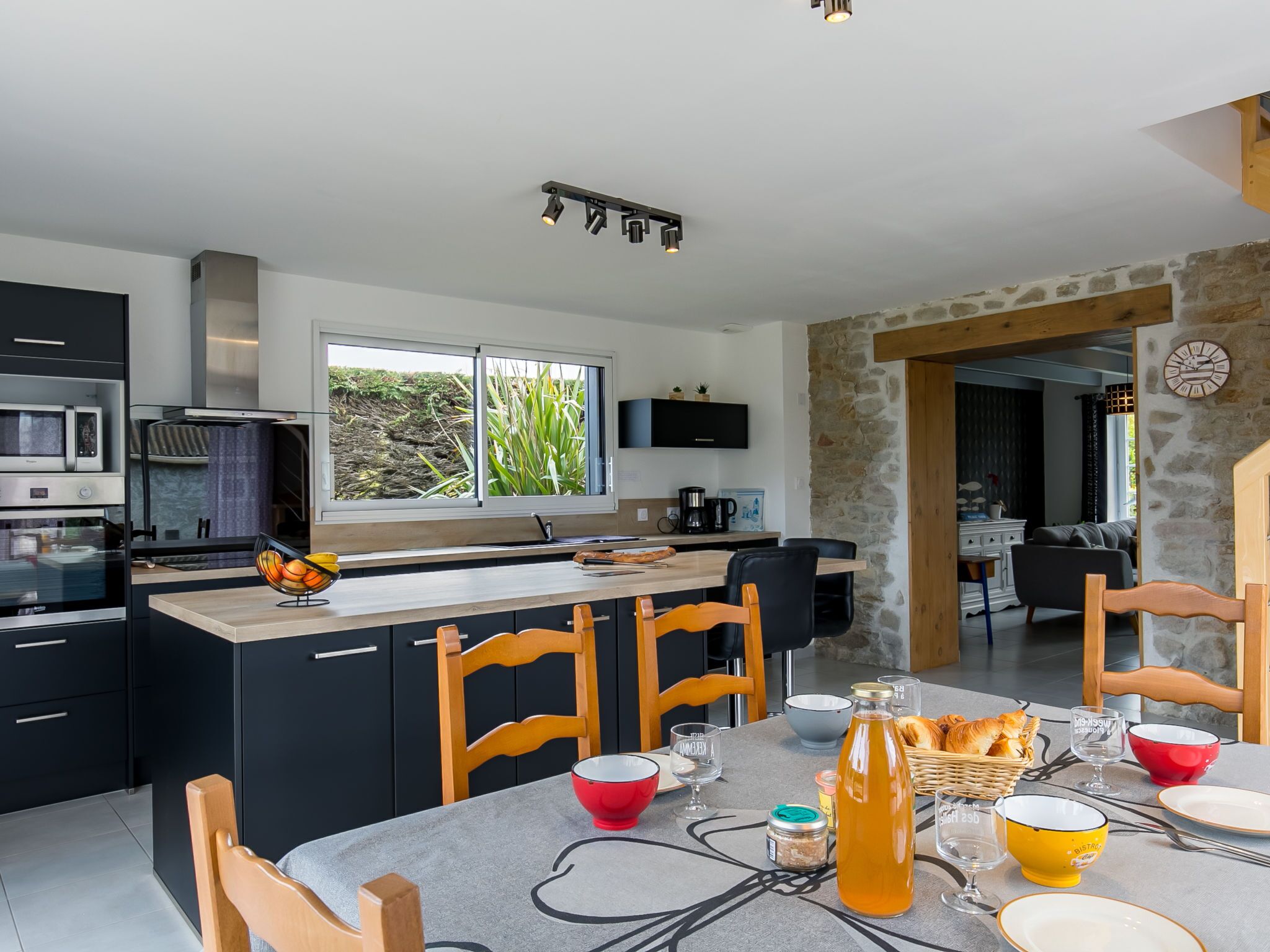 A modern kitchen with a central island, black cabinets, and a stone wall.