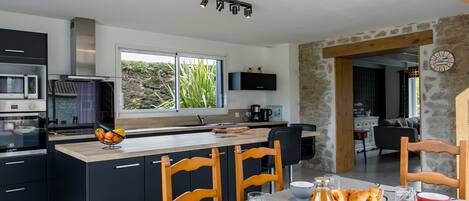 A modern kitchen with a central island, black cabinets, and a stone wall.