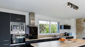 A modern kitchen with black cabinetry, a wooden countertop, a built-in microwave, a stainless steel range hood, and a large window with a view of greenery.
