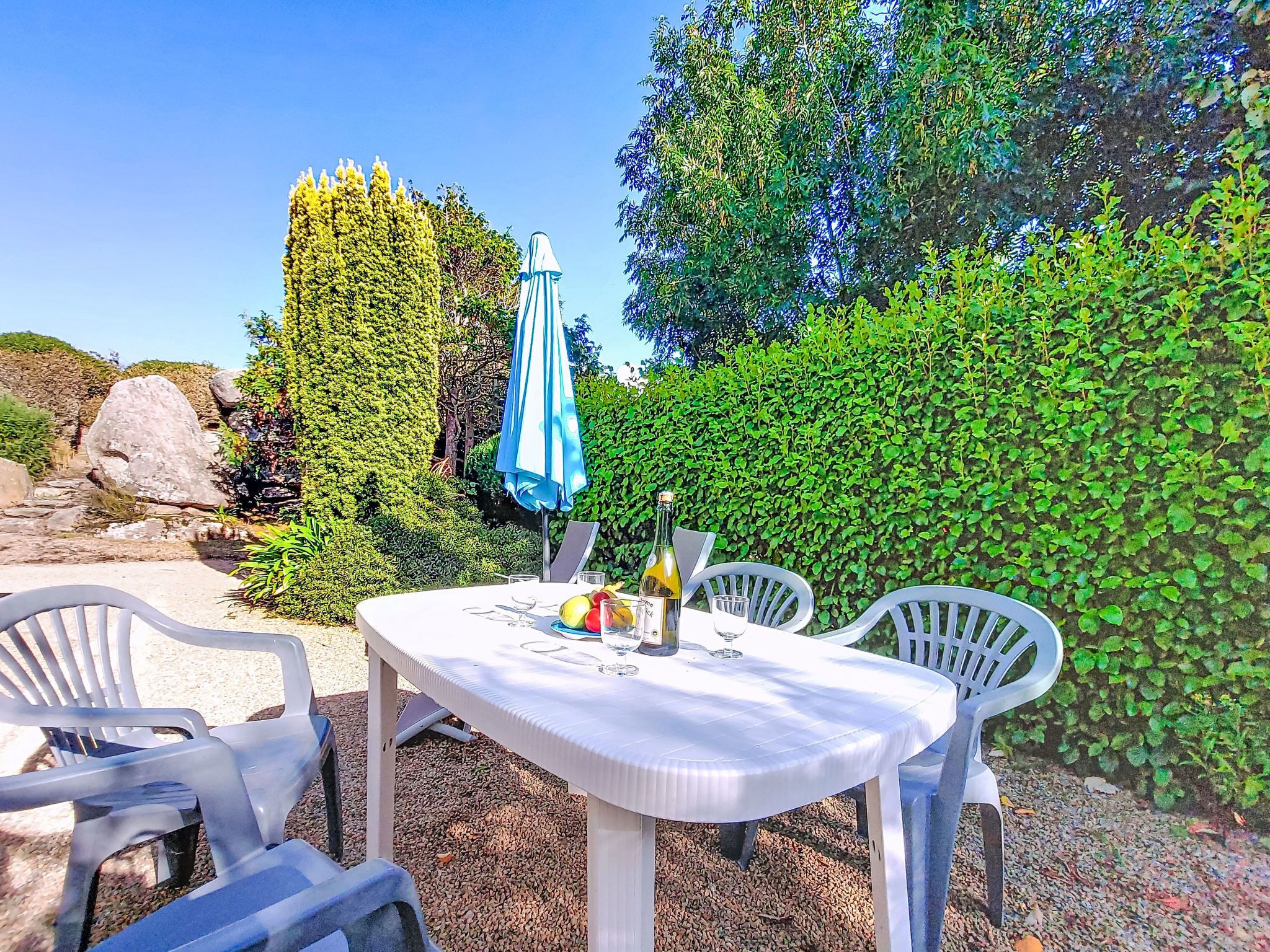 An outdoor dining area with a table and chairs, a bottle of wine, and a blue umbrella.