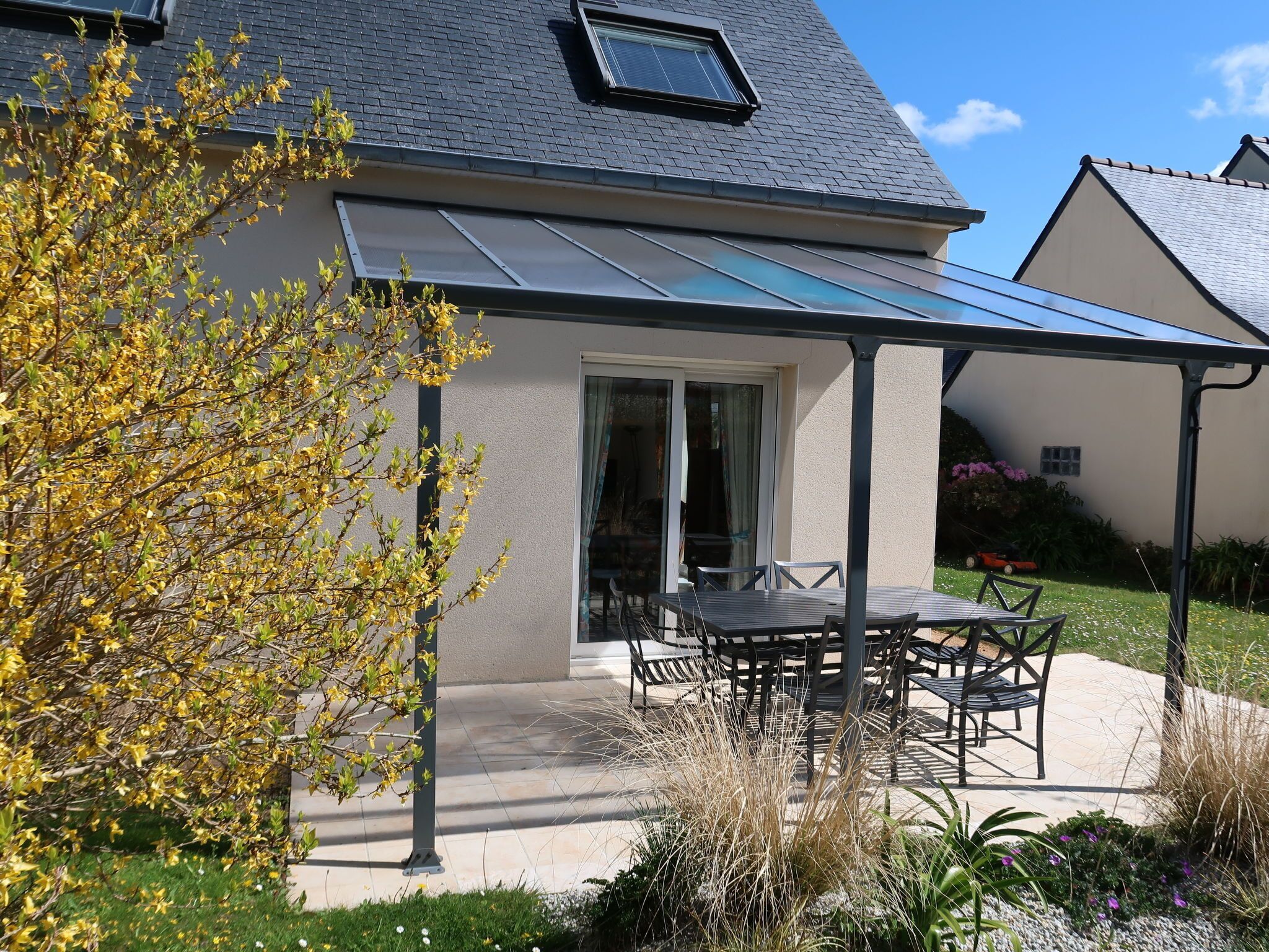A house with a covered patio, a glass door, and a garden with yellow flowering plants.