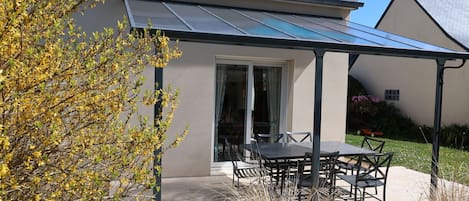 A house with a covered patio, a glass door, and a garden with yellow flowering plants.