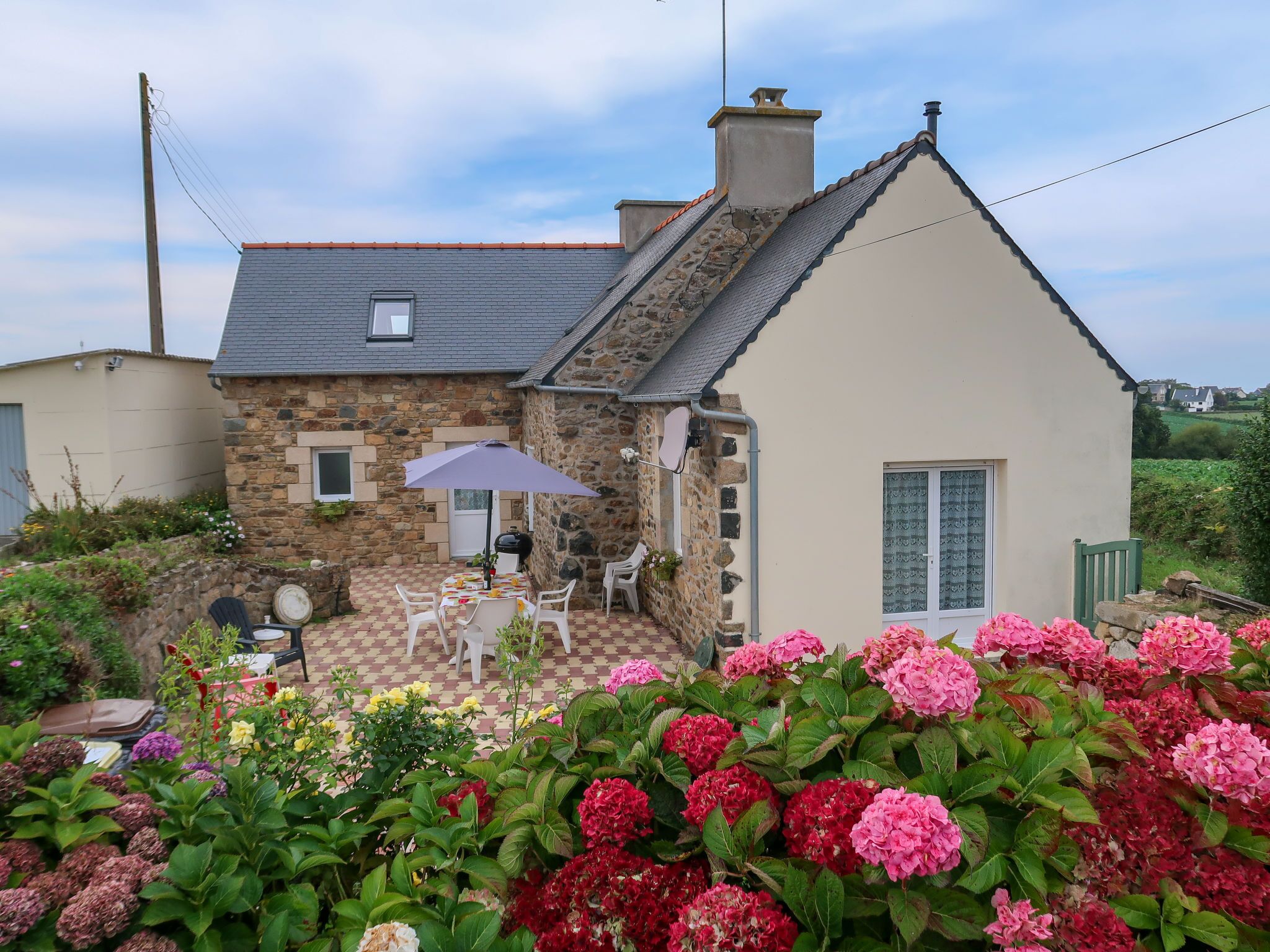 A stone house with a tiled patio, a table with chairs, and a variety of flowers.