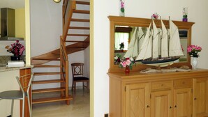 Una escalera de madera que conduce a una plataforma, un armario de madera con un modelo de barco y una silla.