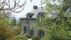 A stone house with a steep roof, surrounded by lush greenery and a clear view of the sea. - Bella Vista by Interhome (Saint Suliac)
