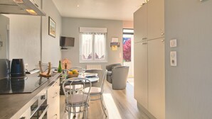 A modern kitchen with a dining area, featuring a built-in stove, a dining table with chairs, and a window with curtains.