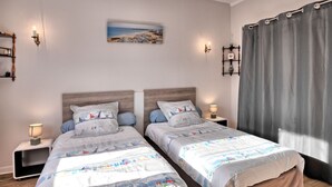 A double room with two beds, each with matching headboards and bedside tables. There is a painting on the wall above the beds, and a window with curtains on the right side.