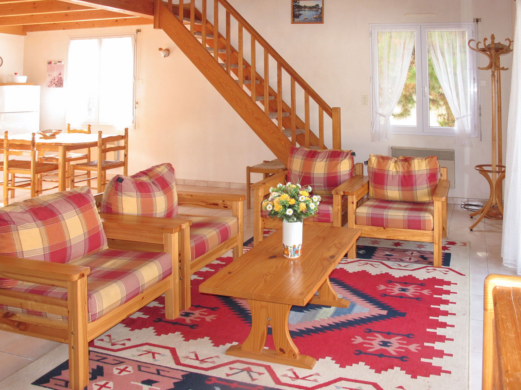 Ein Wohnzimmer mit Holzsitzmöbeln, einer Treppe und einem Fenster mit Vorhängen.