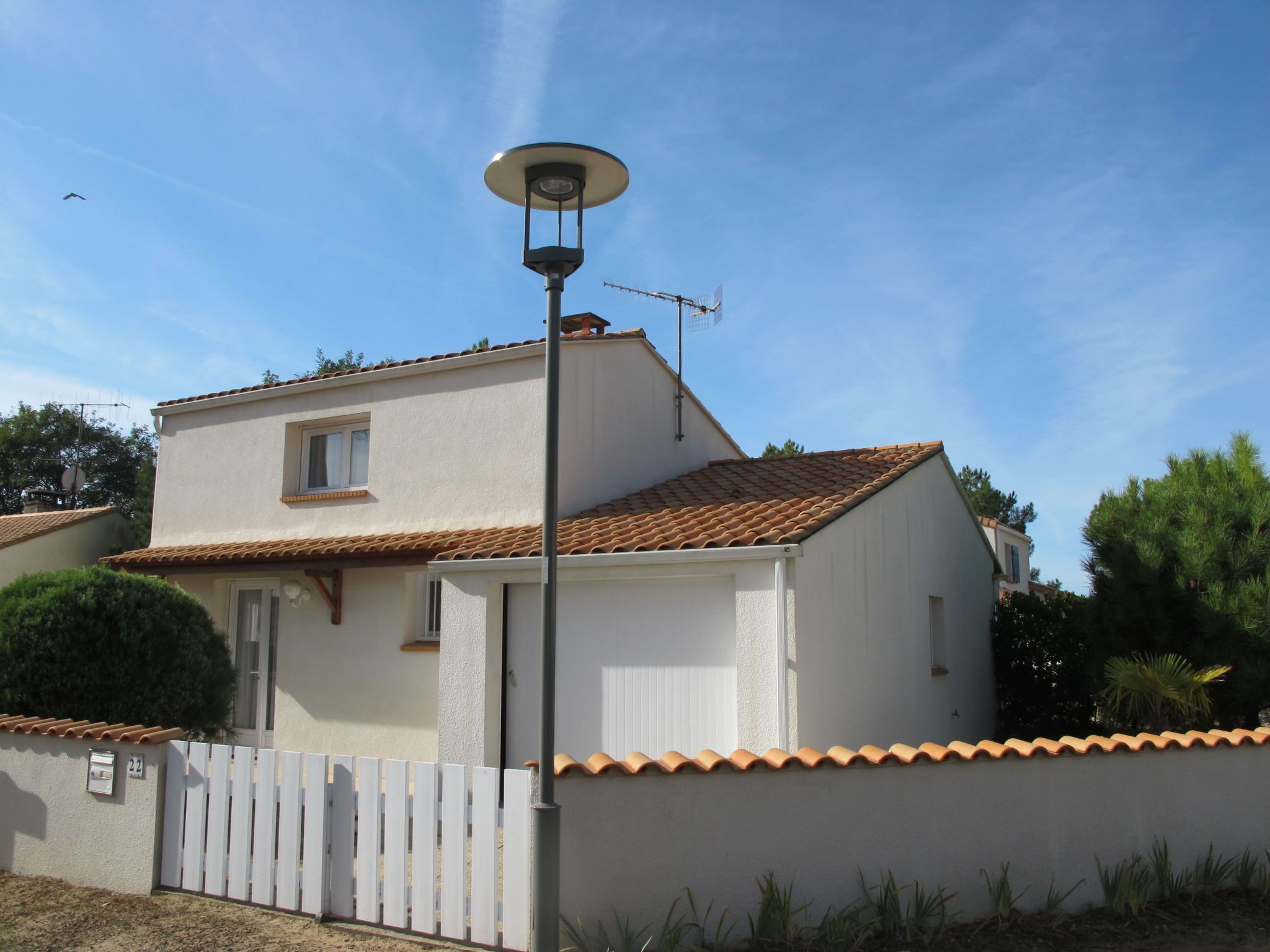 Una casa de dos pisos con techo de tejas, cerca blanca y farola.