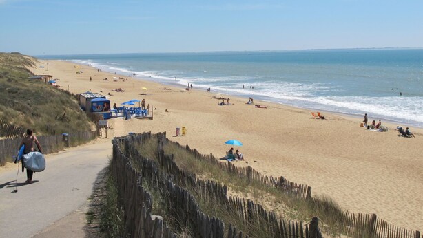 Een strand met een houten omheining, strandstoelen, parasols en mensen die ontspannen.