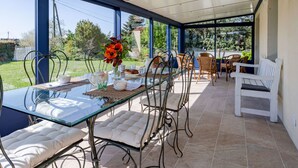 A conservatory with a glass table, cushioned chairs, and a white bench.
