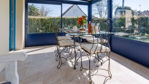 A conservatory with a glass table and chairs, a vase with flowers, and a view of the outside.