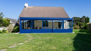 A blue house with a tiled roof, large windows, and a grassy yard.