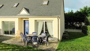 A two-story house with a tiled roof, a covered patio with a table and chairs, and a sliding glass door leading to a covered outdoor area. - Vacation home Néroli by Interhome (Hauteville sur Mer)