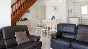 A living room with two black leather sofas, a white coffee table, and a wooden staircase. - Vacation home Néroli by Interhome (Hauteville sur Mer)