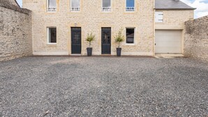 En toetages bygning i sten med grusindkørsel, garage og to krukker med planter foran.