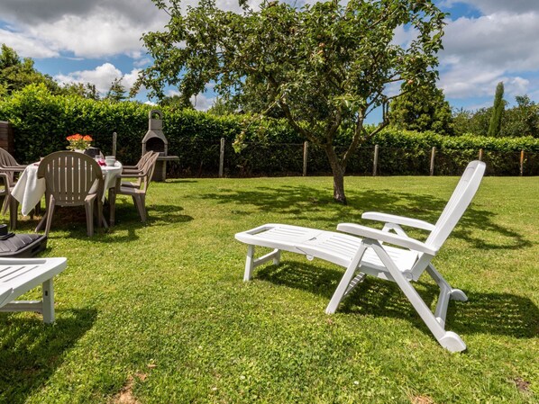A well-maintained outdoor area with a lawn, a white lounge chair, and a table with chairs. - Le Repos by Interhome (Commes)