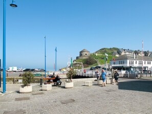 A coastal town with a historic fort on a hill, a paved promenade with benches, and a building labeled "Office de Tourisme". - Le Repos by Interhome (Commes)