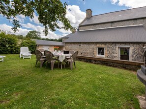 A stone house with a grassy yard, a table with chairs, and a white chair. - Le Repos by Interhome (Commes)
