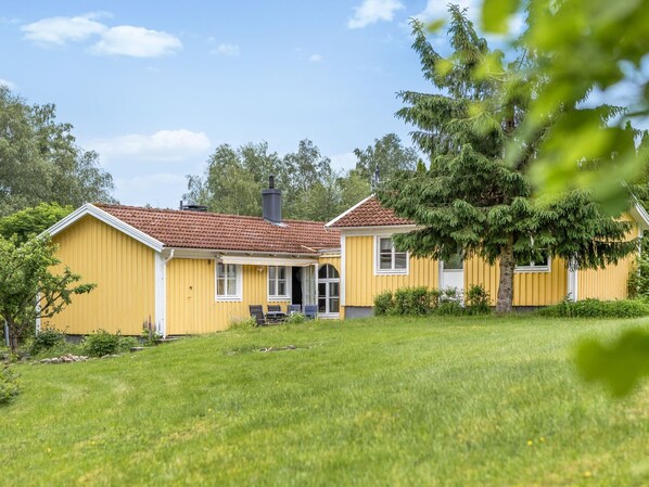 A yellow house with a red-tiled roof, a chimney, and a porch with two chairs. - Kvarnfallet by Interhome (Ullared)