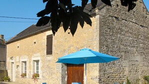 A stone building with a wooden door and windows, a blue umbrella, and blue chairs around a table. - Le Clos Renard by Interhome (Commes)