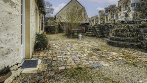 A courtyard with cobblestone flooring, a wooden table with chairs, and stone walls. - Les Lutins by Interhome (Commes)