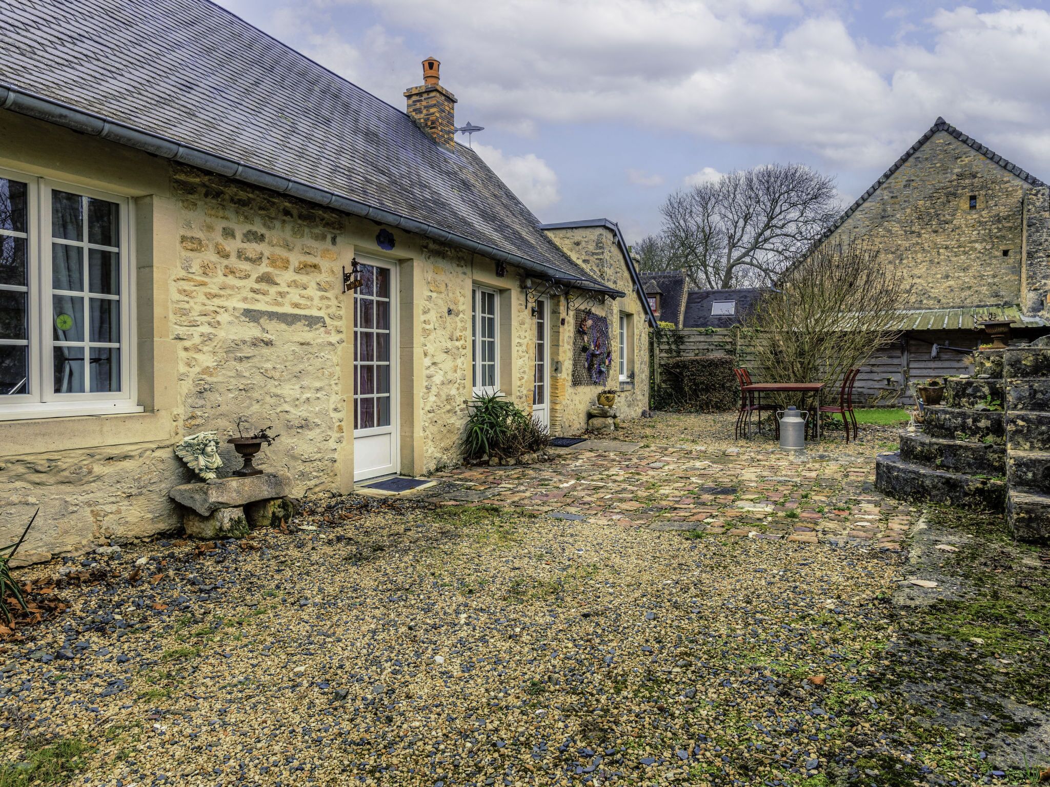 Une maison en pierre avec une allée en gravier et une clôture en bois.