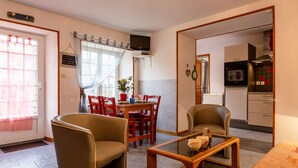 A cozy living room with a sofa, a glass coffee table, and a dining area with a table and chairs. - Les Lutins by Interhome (Commes)