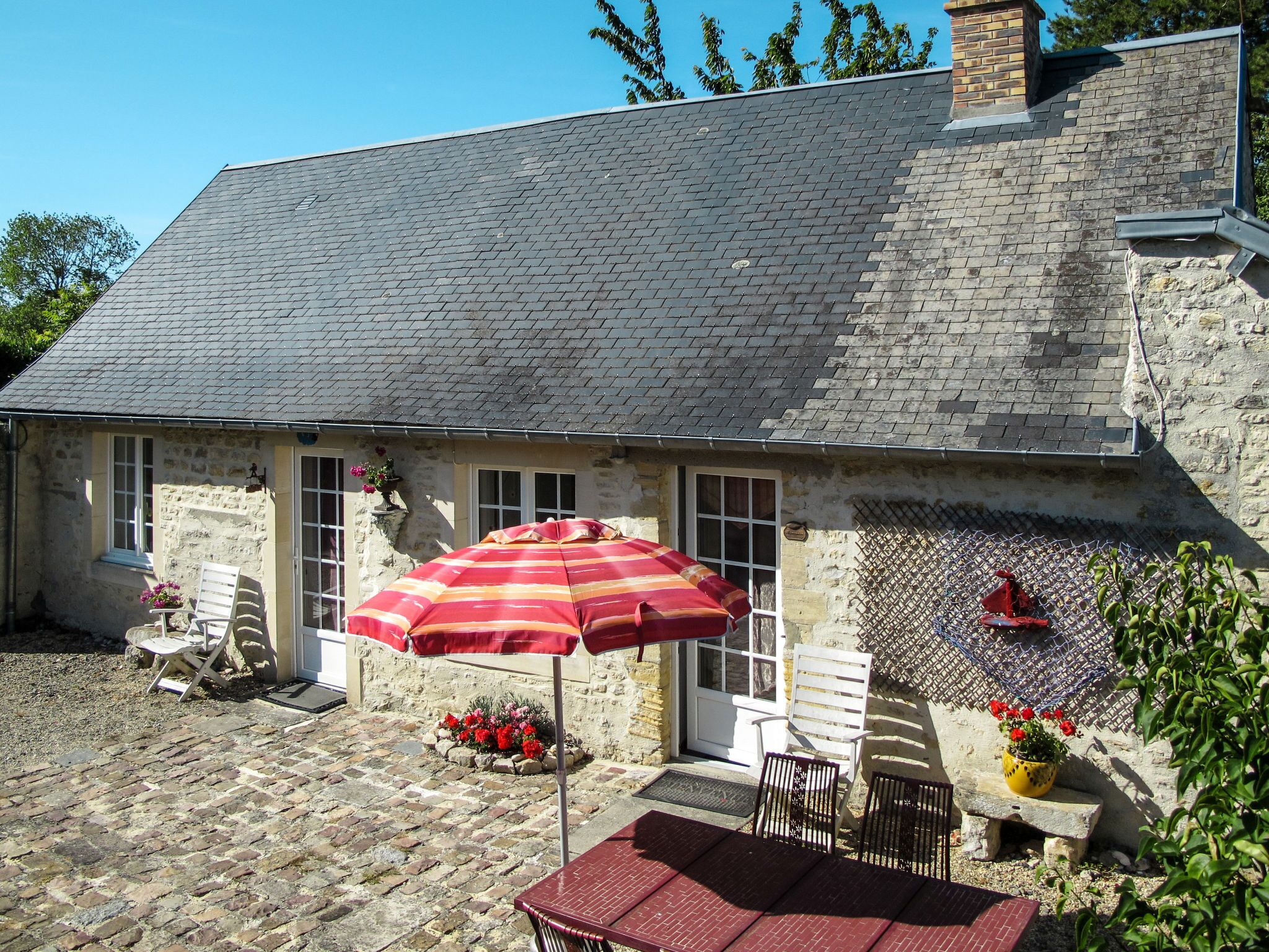 A stone building with a tiled roof, a patio with a table and chairs, and a red umbrella.